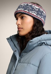 Neulottu pääpanta, jossa on sinisiä, valkoisia ja punaisia kuvioita. Pehmeä, teksturoitu kangas; käytetty vaaleansinisessä toppatakissa, jossa on vetoketjullinen etuosa.