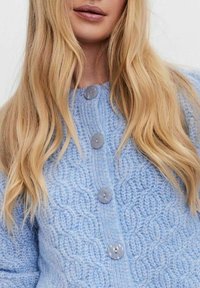 Ljusblå stickad cardigan med ett texturerat mönster, runda grå knappar och en hög halsdesign. Mjuk och mysig textur.