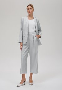 Lys grå dress med smalstripet mønster, som har en skreddersydd blazer og vide bukser. Kombinert med en hvit topp og høye hæler med spiss tå og sølvdetaljer.