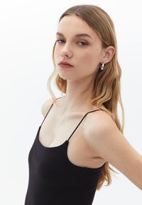 Vestito nero a coste con spalline sottili, caratterizzato da una silhouette aderente e una texture morbida, ambientato su uno sfondo neutro.