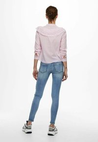 Camicia rosa chiaro con collo arricciato e polsini aperti, abbinata a jeans attillati blu chiaro. Stilizzata con sneaker grigie e bianche.