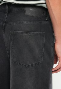 Black denim jeans with a back pocket, featuring a textured finish and a stitched design. Label displays "ONLY & SONS" in black.