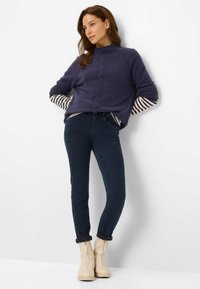 Marineblå sweater med kabelstrik-detalje og stribede ærmer, parret med mørke skinny jeans og beige lynlåse ankelstøvler.