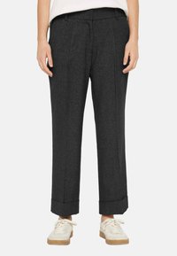 Dark gray, tailored trousers with a textured fabric, featuring front pleats and rolled cuffs, paired with light-colored, casual sneakers.