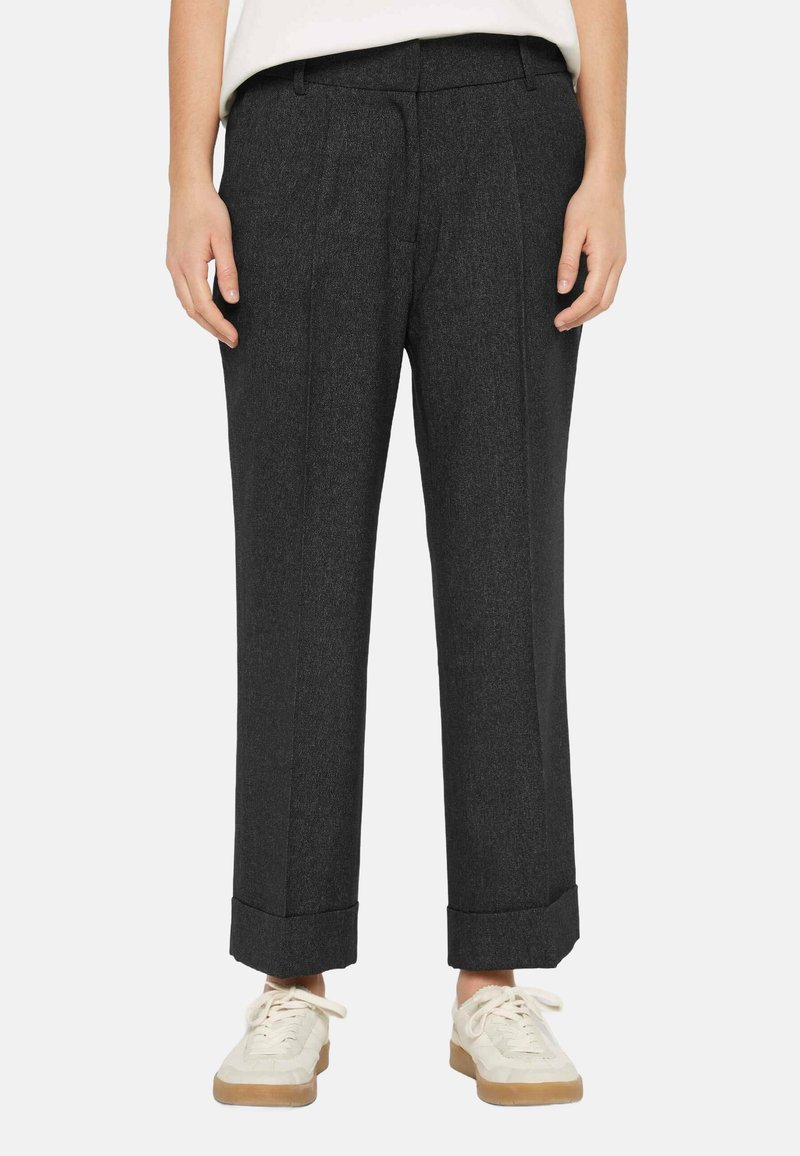 Dark gray, tailored trousers with a textured fabric, featuring front pleats and rolled cuffs, paired with light-colored, casual sneakers.