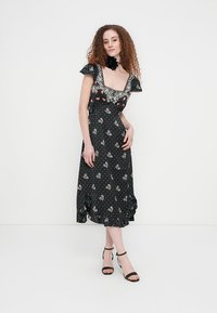 Μαύρο φόρεμα με λουλουδένιο μοτίβο, κοντά μανίκια με βολάν, δαντελένιο τελείωμα και πουά σχέδιο. Το τελείωμα του φορέματος έχει βολάν. Συνδυάζεται με μαύρα σανδάλια.