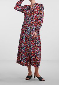 Kukkakuvioinen maksimekko, jossa on pitkät hihat, napillinen kaula-aukko ja kerroksittainen helma, kirkkaissa väreissä mustalla pohjalla.