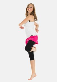 Rosa Sportshorts, kombiniert mit schwarzen Leggings, getragen zu einem weißen Tank-Top. Die Shorts haben einen elastischen Bund und seitliche Kordeln.
