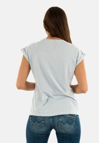 Maglietta a maniche corte blu chiaro con maniche arrotolate. Tessuto di cotone morbido, vestibilità rilassata, scollatura rotonda e design semplice. Indossata con jeans in denim scuro.