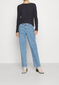 Pull en maille bleu marine, coupe décontractée, col rond. Jeans bleu clair à jambes droites, style classique à cinq poches. Bottines beiges à talon bloc.