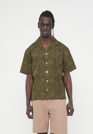 Kratka majica z ovratnikom v olivno zeleni barvi z teksturiranim vzorcem živalskega tiska, ki ima spredaj gumbe in svetlo obarvane gumbe.