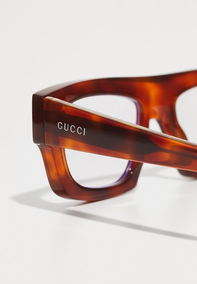Gafas de acetato carey con un audaz marco geométrico, que presentan un logo en plata "GUCCI" en la patilla y lentes con tintado púrpura.