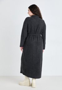 Long gray woolen coat with a belted waist, long sleeves, and a lapel collar, paired with cream platform boots. Back view.