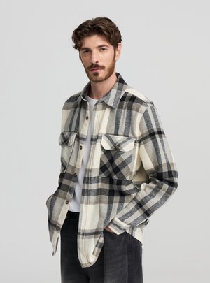 Camicia in flanella a quadri crema e nero con accenti grigi, due tasche sul petto, bottoni sul davanti e colletto classico.
