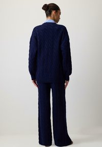 Marineblå kabelstrikket sweater og matchende vide bukser, med et tekstureret mønster, ribbede manchetter og en afslappet pasform.