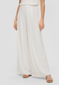 Witte, wijde broek van lichtgewicht stof. Heeft verticale plooien en een hoge taille. Draagt met eenvoudige slippers.