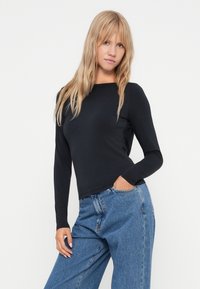 Czarny, długorękawowy top z okrągłym dekoltem, wykonany z miękkiego materiału. W połączeniu z luźnymi, jasnoniebieskimi dżinsami o klasycznym kroju.