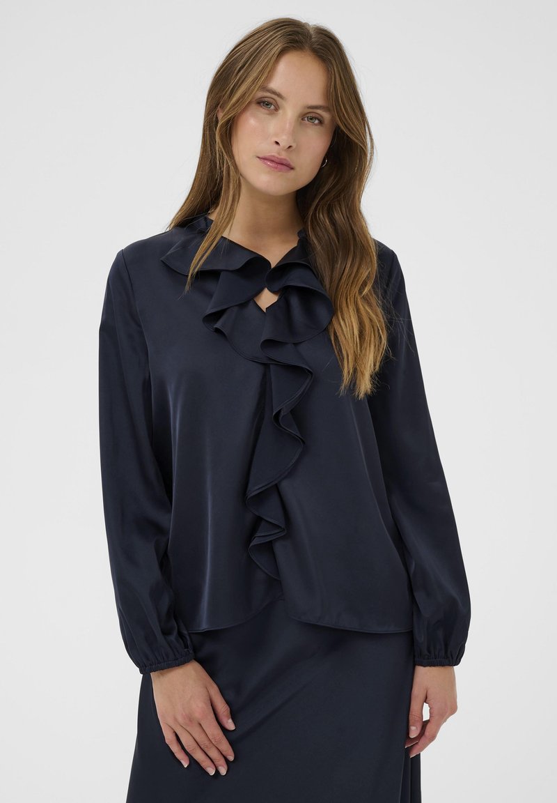 Marineblouse met een gerimpelde halslijn en voorkant, lange mouwen met elastische manchetten, en een gladde textuur. Keyhole-detail bij de hals.