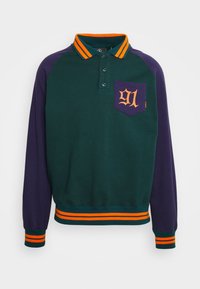 Polo à manches longues vert et violet avec col rayé orange. Présente une poche sur la poitrine avec le numéro "91" en orange. Fabriqué en doux coton.