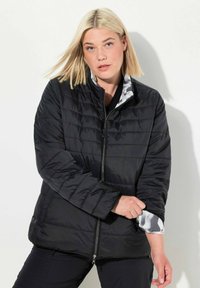 Sort vatteret jakke med høj krave, lynlås lukning og mønstret for, der er synligt ved ærmerne. Har en afslappet pasform og en glat tekstur.