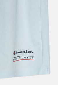 Svetlomodré bavlnené tričko s logom "Champion ATHLETICWEAR" v čiernej a červenej farbe na dolnom ľavom rohu. Hladký povrch, krátke rukávy.