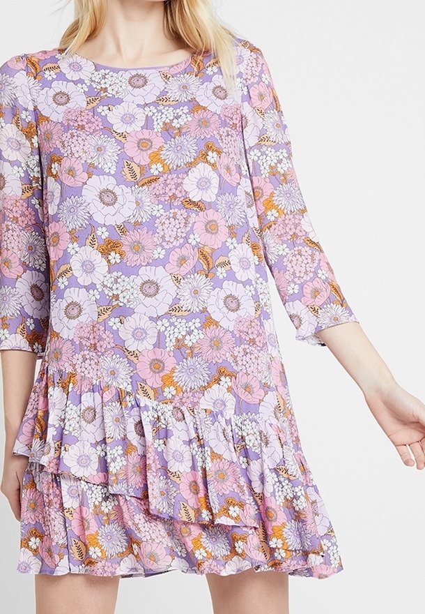 Kukallinen mekko, jossa on liilapohja, kolme neljäsosaa hihat, röyhelöhelma sekä suuria vaaleanpunaisia, valkoisia ja oransseja kukkia ja lehtiä.
