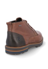 Botas de tobillo de cuero marrón con un tacón oscuro contrastante, diseño de cordones, suela a rayas azules y marrones, y textura suave.