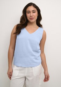 Un haut sans manches bleu clair avec un décolleté en V, confectionné à partir d'un tissu texturé, associé à un pantalon crème ample.