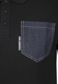 Černé polo tričko s džínovou kapsou na hrudi s žlutým prošitím. Má tři knoflíky u límce. Na kapse je značka výrobce.