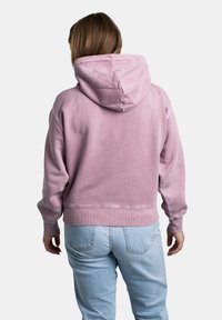 Haut en rose pâle, à coupe courte, avec une coupe décontractée, une texture douce et une capuche avec cordon de serrage. Assorti avec un jean en denim bleu clair.