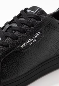 Sneaker en cuir noir avec une tige texturée, des lacets noirs et un logo blanc. Dispose d'une semelle en caoutchouc lisse et de détails de couture subtils.