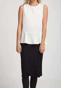 Top blanco sin mangas con peplum y tela texturizada, combinado con una falda negra ajustada, creando un conjunto bicolor y contrastante.