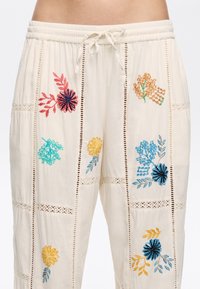 Leichte cremefarbene Hose mit buntem Blumenstickerei in Blau, Rot, Gelb und Grün. Enthält Spitzendetails entlang der Nähte. Elastischer Bund.