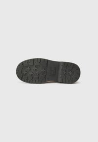 Semelle en caoutchouc noir d'une chaussure, présentant un motif texturé pour l'adhérence, placée sur un fond blanc uni.