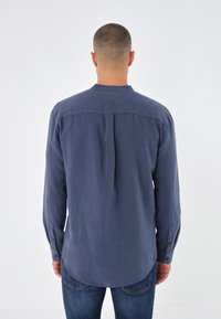Marineblaue Langarmbluse aus leichtem Stoff, mit abgerundetem Saum, rückseitiger Falte und knöpfbaren Manschetten.