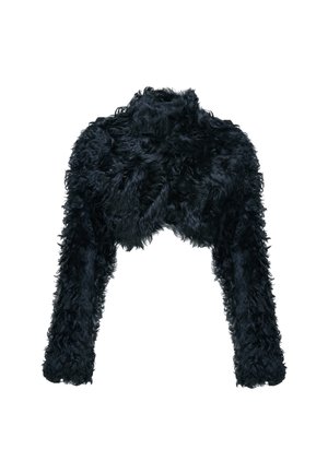 Femme portant une longue robe noire fendue à la cuisse, une veste en fourrure noire texturée, des bottes noires, et tenant un sac à main noir avec une chaîne dorée.