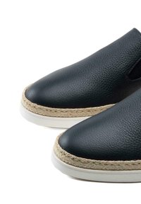 Chaussures en cuir noir à enfiler avec une surface texturée, dotées d'une bordure en corde naturelle et d'une semelle en caoutchouc blanc. Design à bout arrondi.