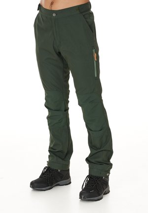 Groene outdoorbroek met een slim fit, gemaakt van robuust materiaal. Bevat een zij-ritszak en versterkte knieën, gecombineerd met zwarte boots.