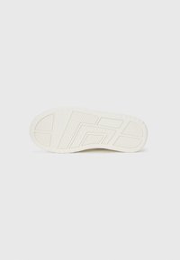 Semelle d'une sneaker, présentant un matériau en caoutchouc blanc crémeux texturé avec des motifs géométriques et des rainures pour la traction.