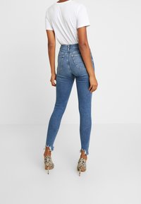 Úzké džíny z světle modrého denimu s vysokým pasem, ošuntělým lemem a zadními kapsami, doplněné vzorovanými lodičkami na vysokém podpatku.