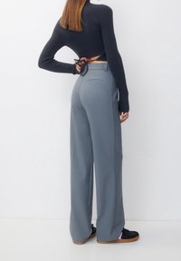 Grijze wijde broek met een gladde textuur, voorzien van een achterzakdetail, gedragen met een marineblauw geribbelde trui. De outfit wordt compleet gemaakt met zwarte schoenen.