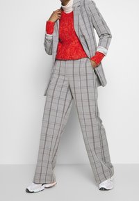 Pantalon à carreaux gris avec des jambes larges, associé à un pull en tricot rouge texturé avec des poignets blancs. Chaussures : baskets blanches avec des accents colorés.