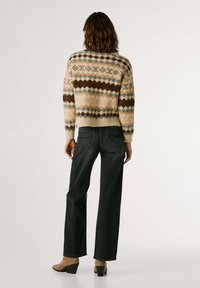 Gebreide trui in crème met multicolor geometrische patronen; gecombineerd met donker rechte jeans en tan kleurige haklaarzen.