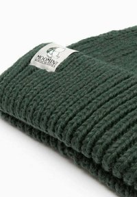 Tummanvihreä ribbiknitti pipo, jossa on käännevarsi ja valkoinen etiketti, jossa on sarjakuvahahmo sekä teksti "MOOMIN BY NORDICBUDDIES."