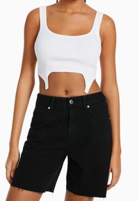 Bílý žebrovaný crop top se čtvercovým výstřihem a unikátním výřezem, doplněný o černé džínové šortky s vysokým pasem, zdobené třepeným lemem a kapsami.