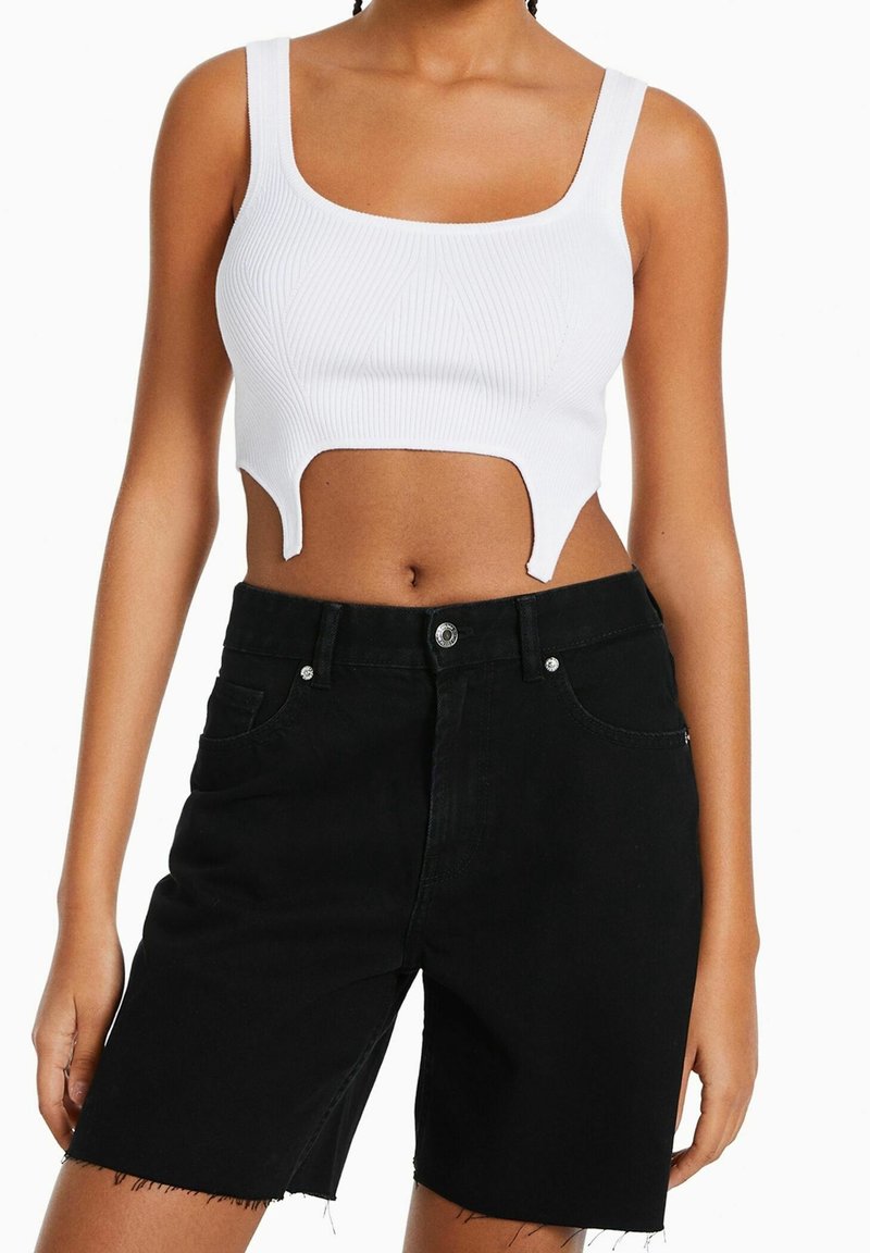 Bílý žebrovaný crop top se čtvercovým výstřihem a unikátním výřezem, doplněný o černé džínové šortky s vysokým pasem, zdobené třepeným lemem a kapsami.