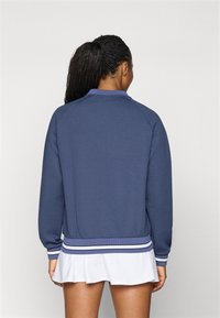 Donkerblauwe sweatshirt met ribgebreide mouwen en onderrand. Heeft een ronde hals en een geweven stof, gecombineerd met een witte klokrok.