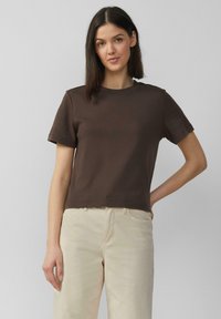 T-shirt marron à manches courtes avec un col rond, fabriqué en coton doux. Coupe droite avec des détails de couture minimaux, associé à un pantalon créme léger.