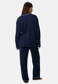 Marineblå sæt med pyjamas lavet af blødt stof; har lange ærmer, en krave og hvid piping på manchetter og krave.
