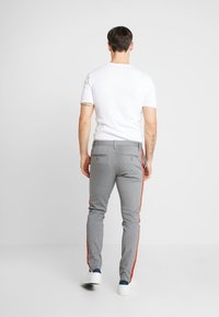 Szare spodnie z czerwonymi bocznymi paskami, o wąskim kroju. Materiał z mieszanki bawełny. Połączone z prostą białą koszulą z krótkim rękawem i białymi trampkami.